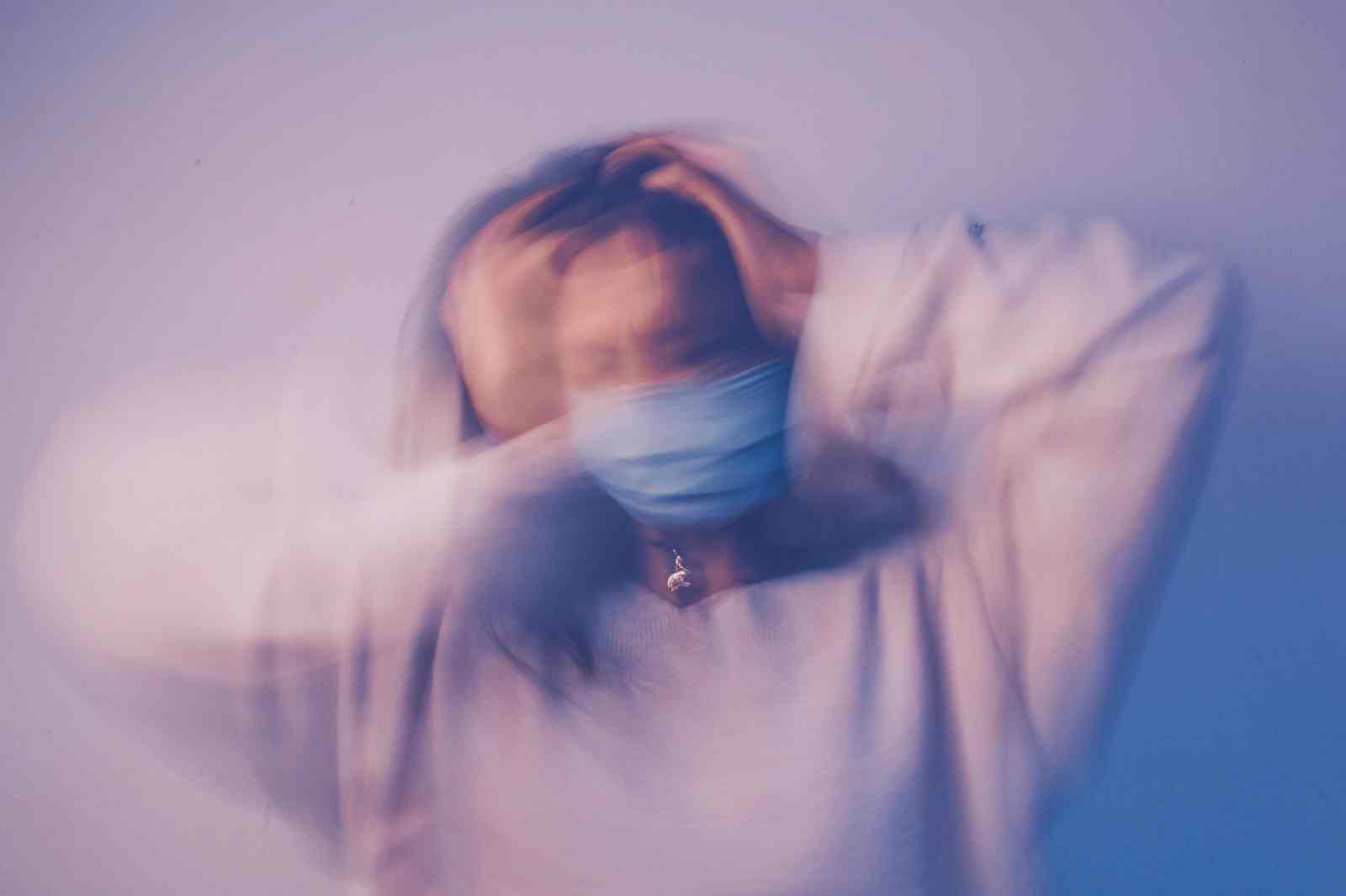 A blurry, distorted image of a person in a mask holding their head.