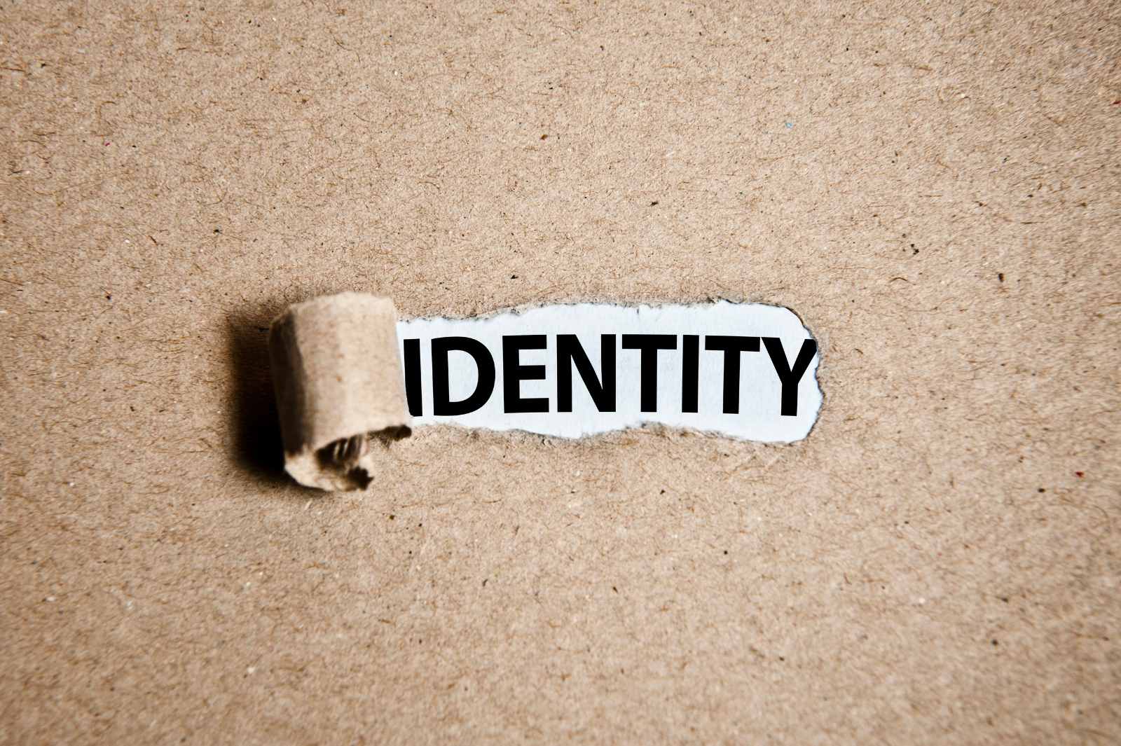 The word "IDENTITY" revealed through a torn hole in brown paper.