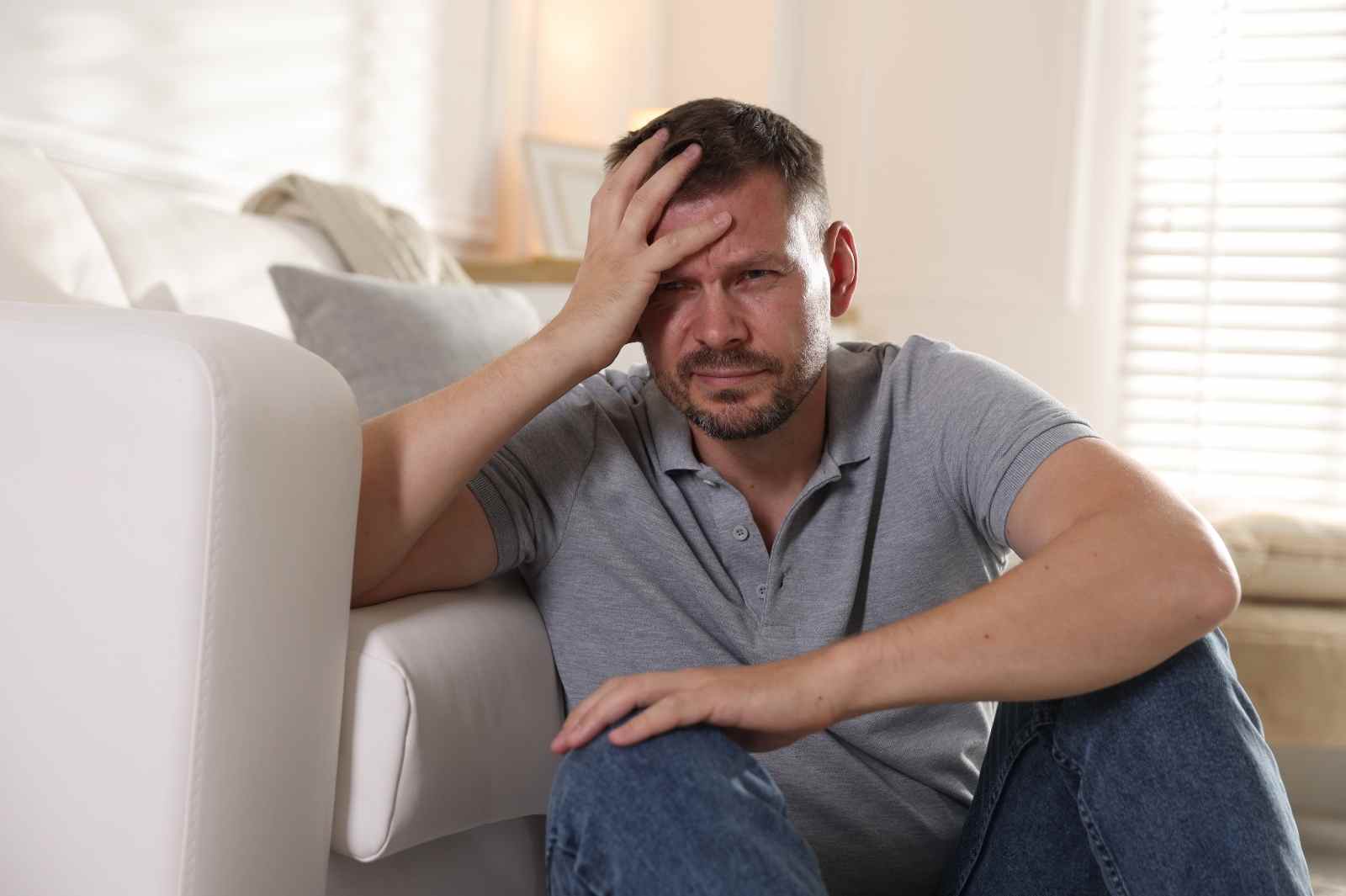 Man sitting on floor with hand on head, looking distressed