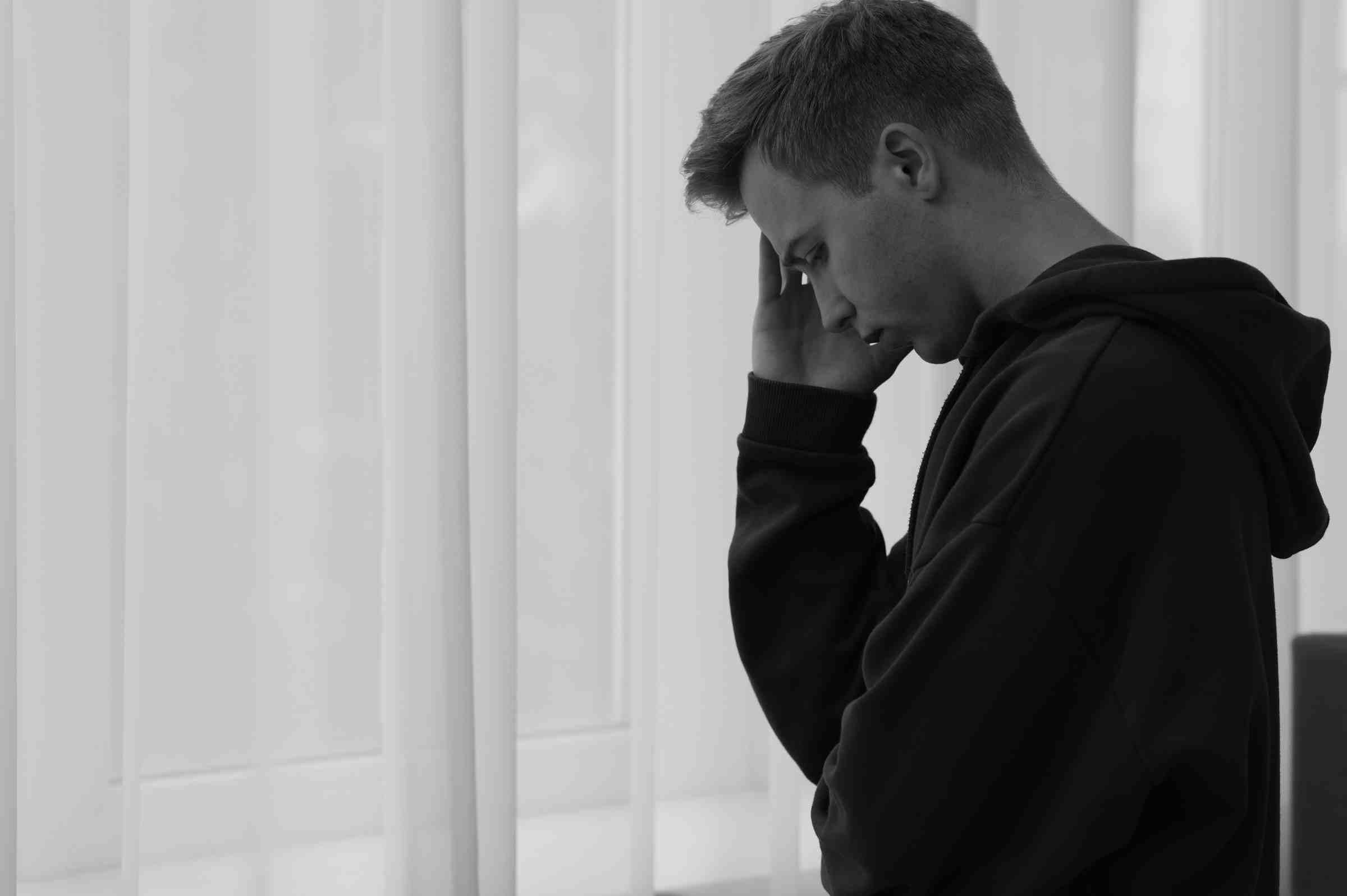Man standing by window holding head, looking stressed