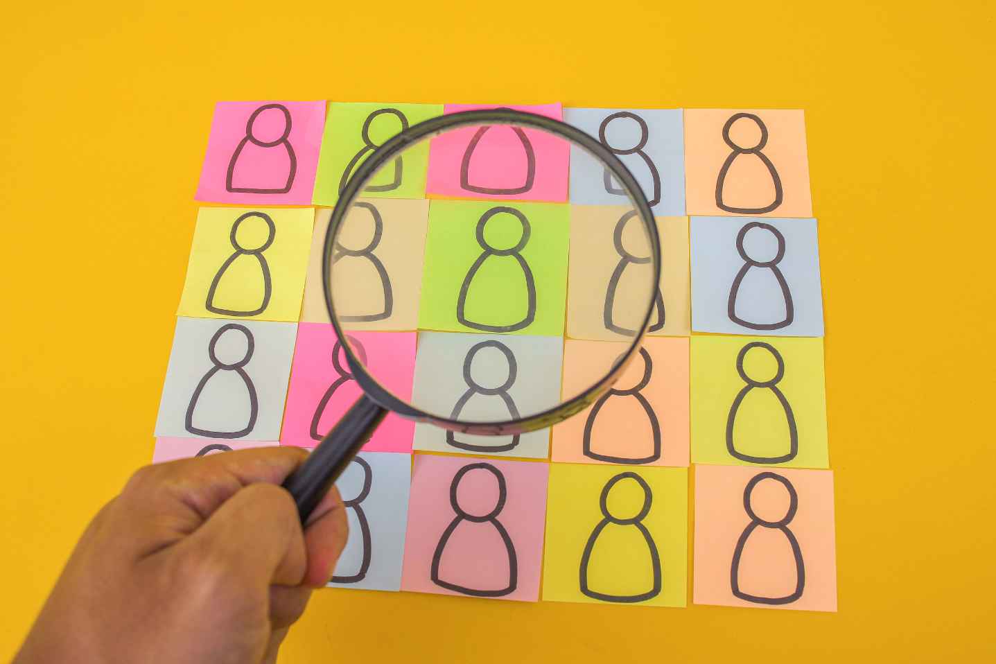Magnifying glass focusing on one person icon among many on colorful notes.