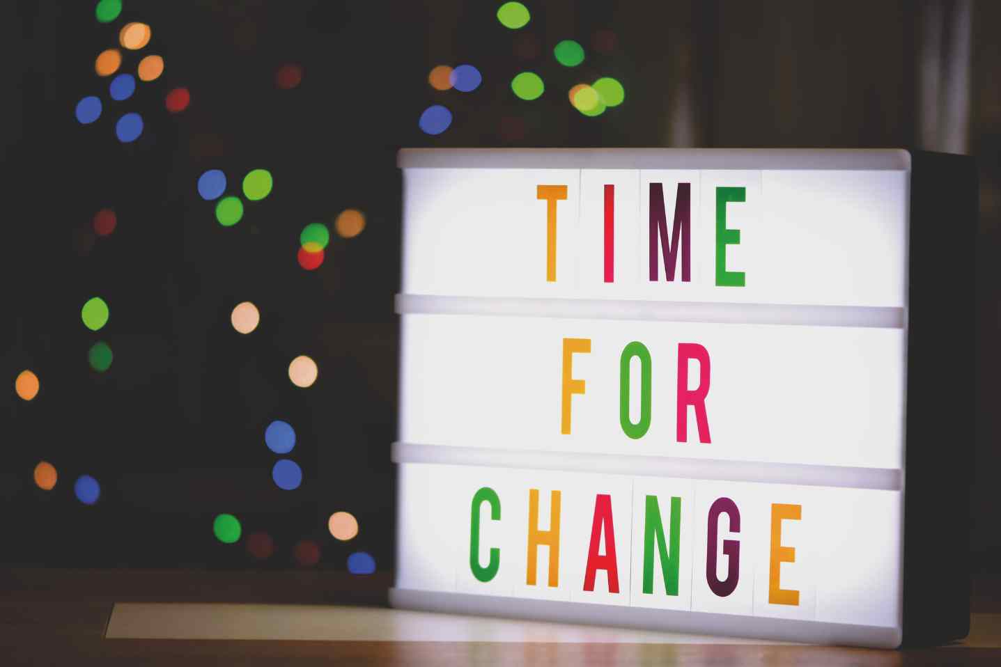 Lightbox sign displaying “Time for change” with colorful lights in background.