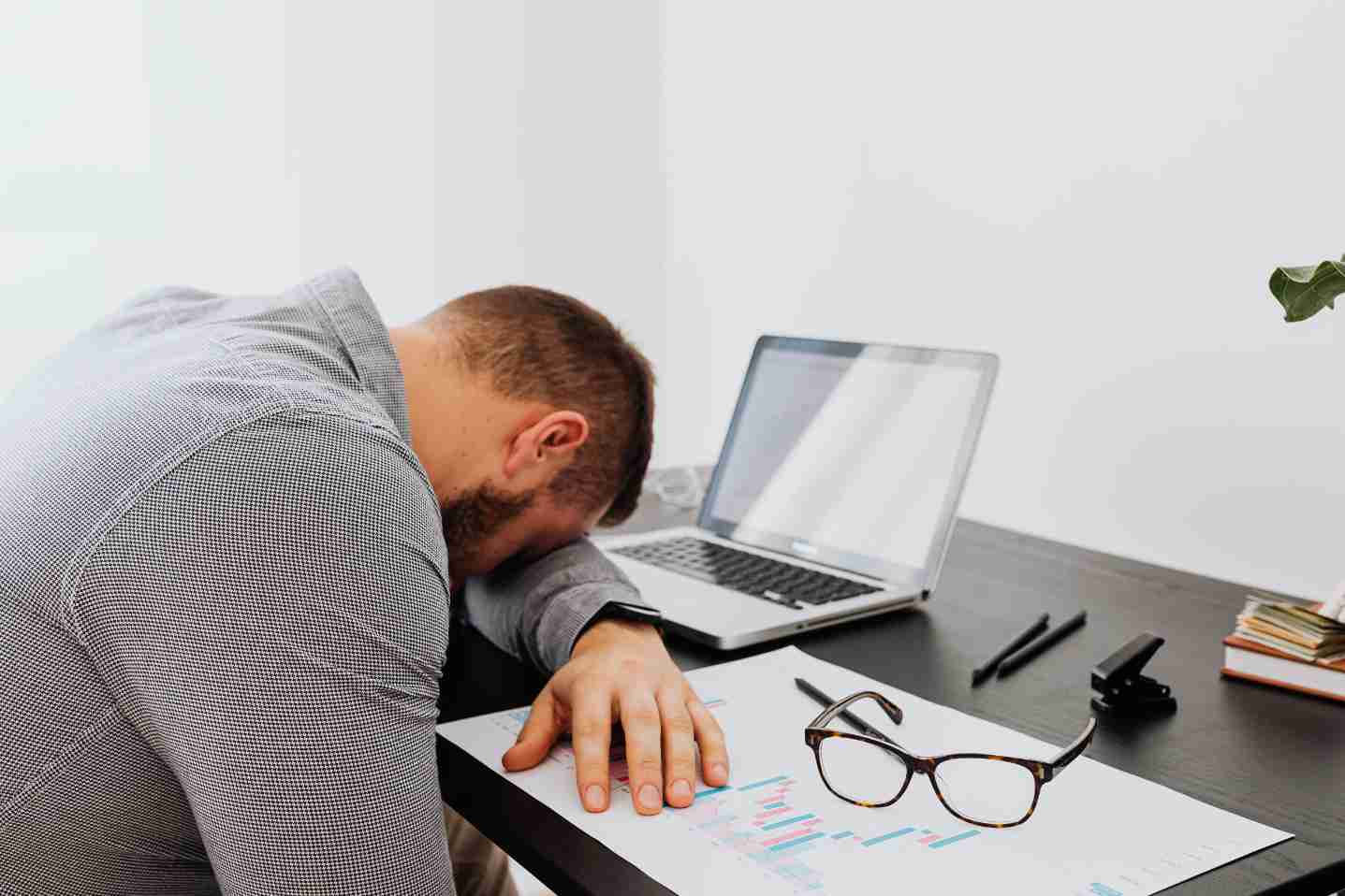Person asleep at desk beside laptop and papers, showing fatigue.