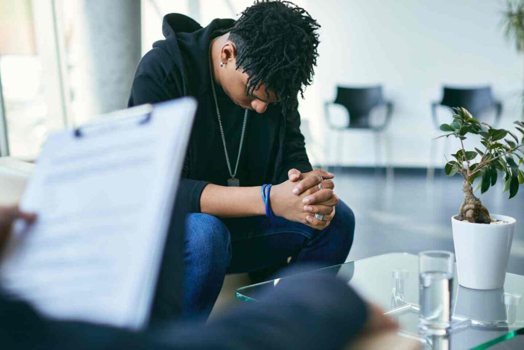 Person sitting with head down and hands clasped in a counseling session.