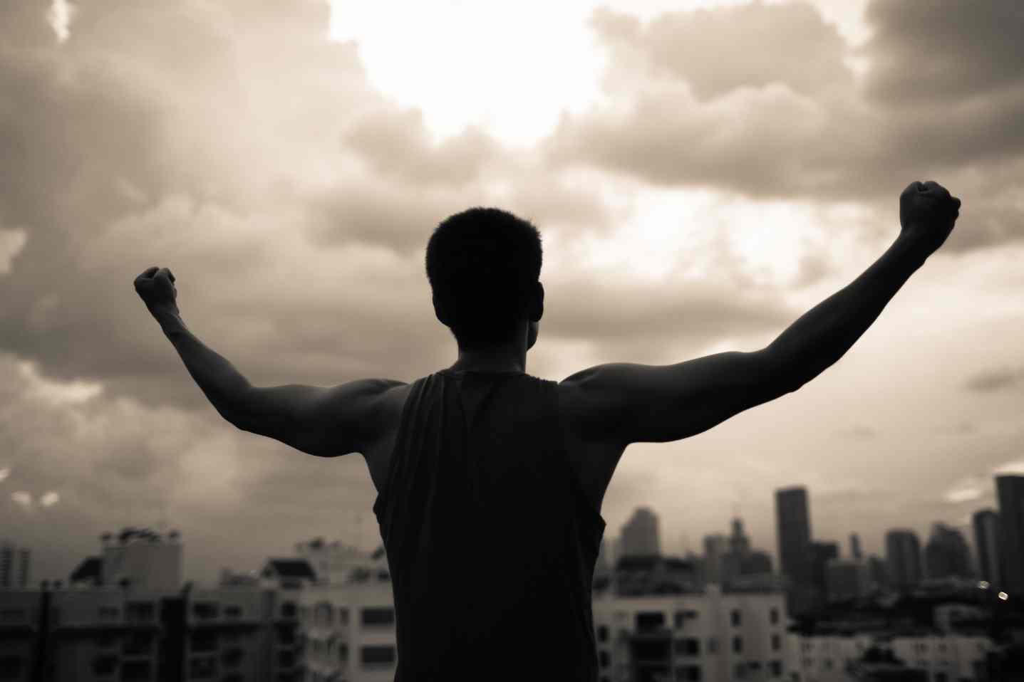 Silhouette of person raising arms triumphantly over city skyline.