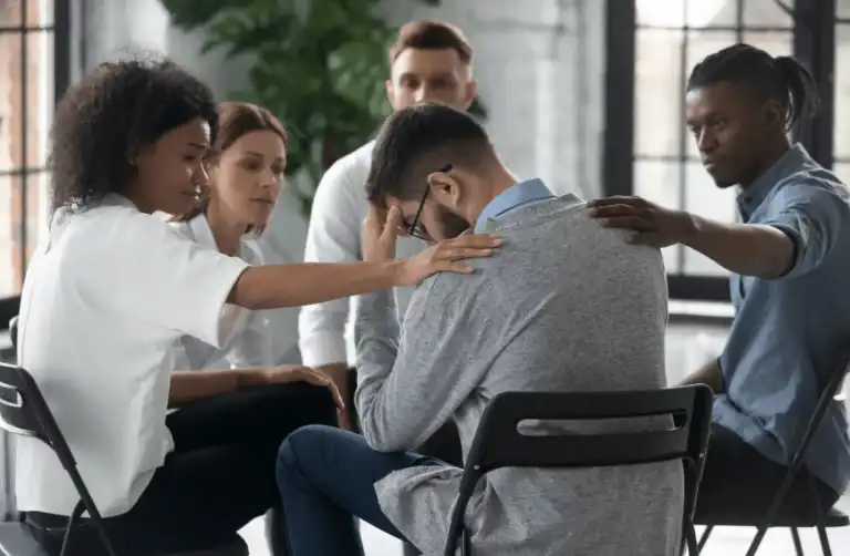 Group sitting in a circle comforting a man during grief counseling